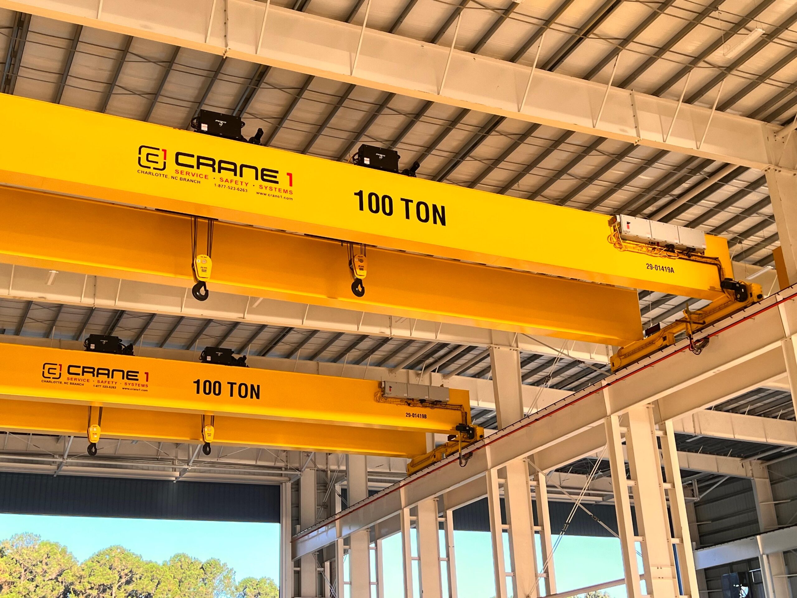 Two yellow industrial overhead cranes marked "100 TON" are installed inside a large metal warehouse, with steel beams and roof panels visible.